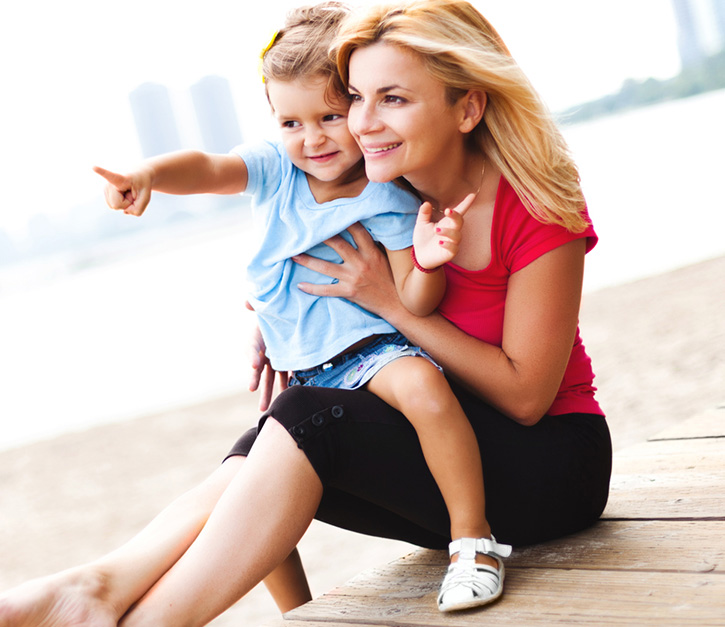 Mother and daughter spending time together at the beach, sitting on a boarwalk. Daughter is showing something to the mother.